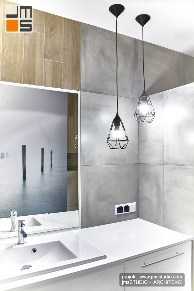 Jasne lakierowane meble łazienkowe w połączeniu z szarą płytką gresową dużym lustrem i nowoczesnymi czarnymi lampami we wnętrzu łazienki