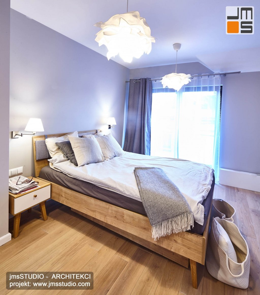 Przestronna sypialna w stylu skandynawskim to pomysł na duże szare łóżko z jasnego drewna w szarym wnętrzu 